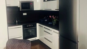 Eine moderne Küche mit weißen Schränken, einer schwarzen Arbeitsplatte, einem Edelstahl-Kühlschrank und einer Mikrowelle.