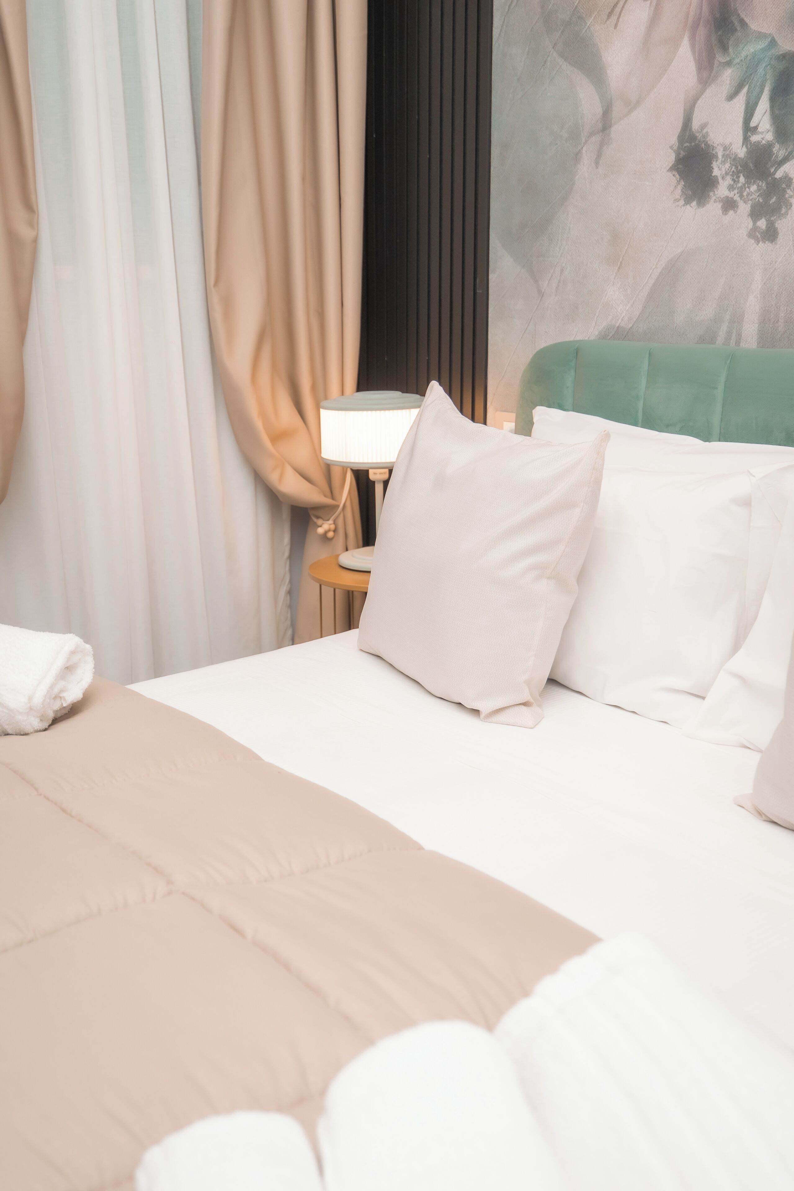 A neatly made bed with white linens and a beige throw blanket, a bedside table with a lamp, and a wall with a textured pattern.