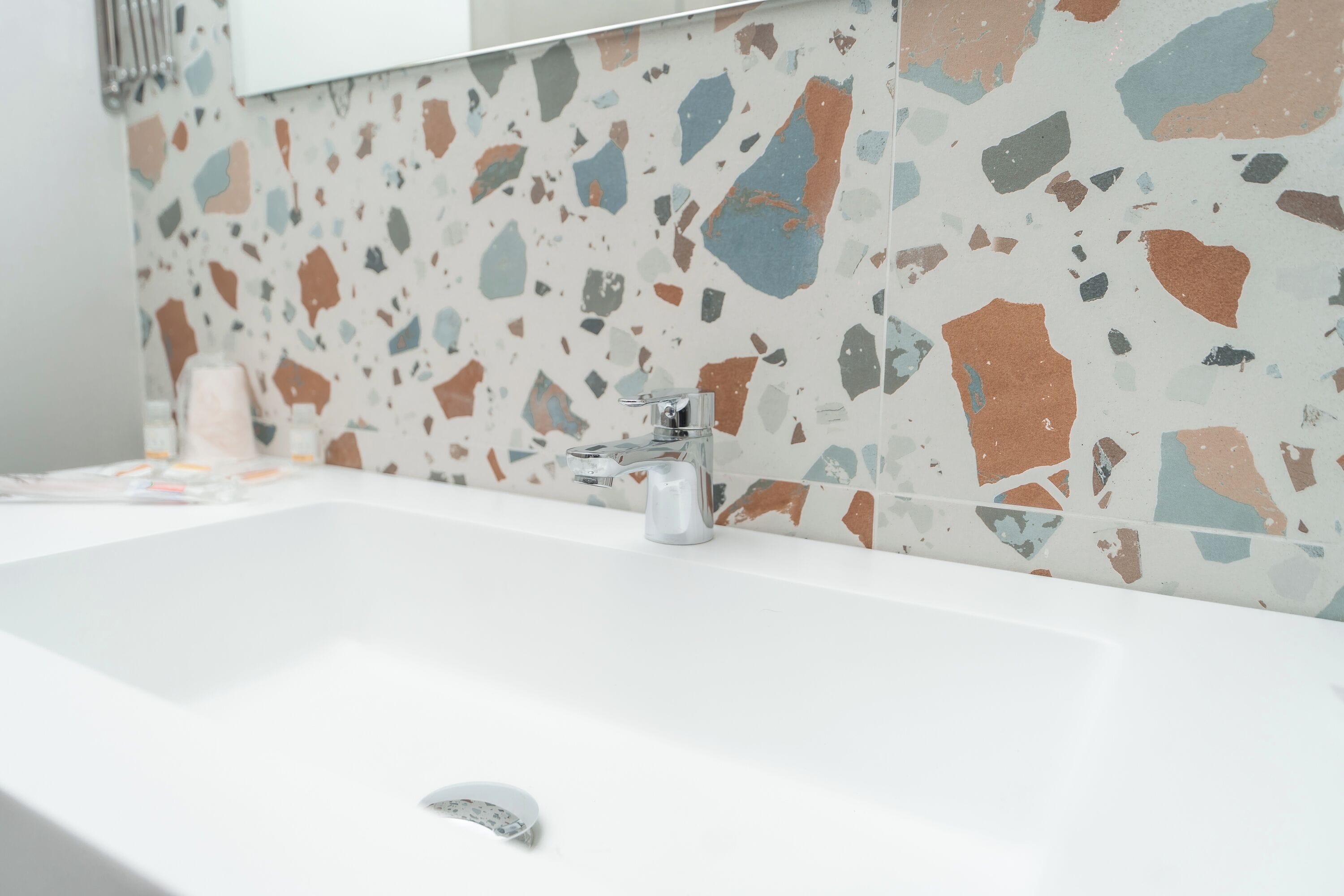 A bathroom with a white sink, a modern faucet, and a terrazzo tile backsplash.