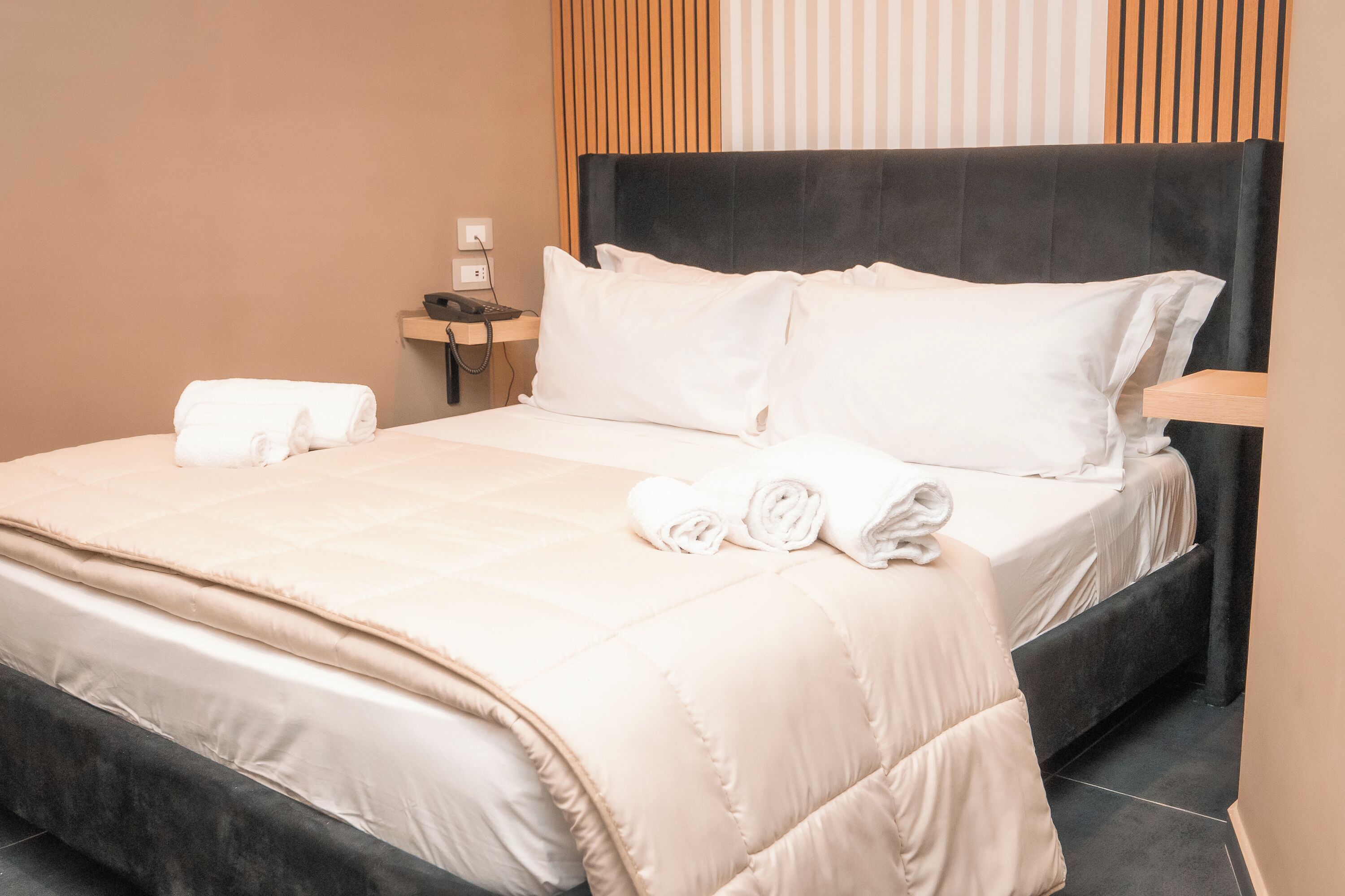 A neatly made bed with a beige duvet, two pillows, and rolled towels.
