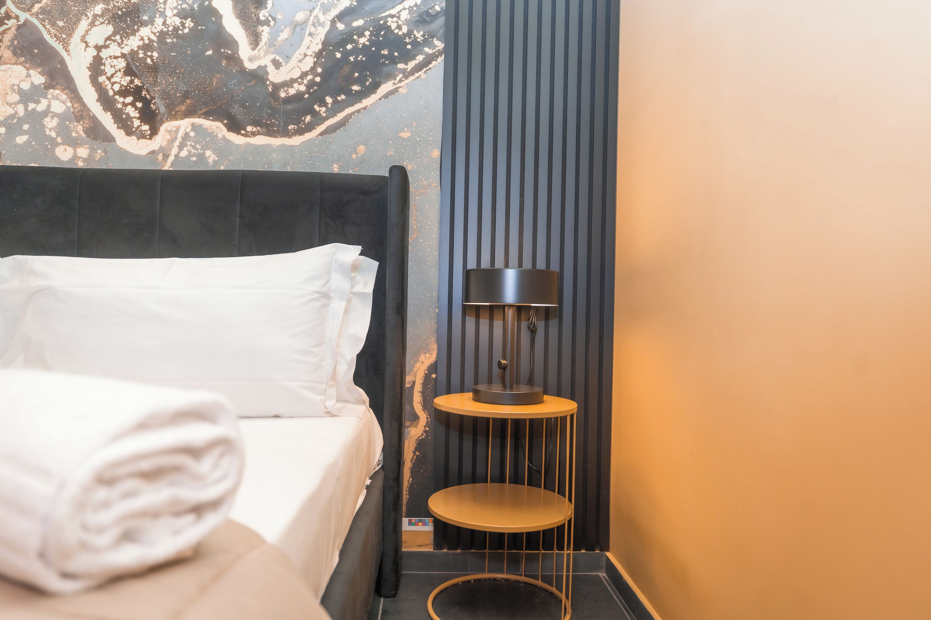 A neatly made bed with white linens, a black headboard, and a wall with a marbled design.