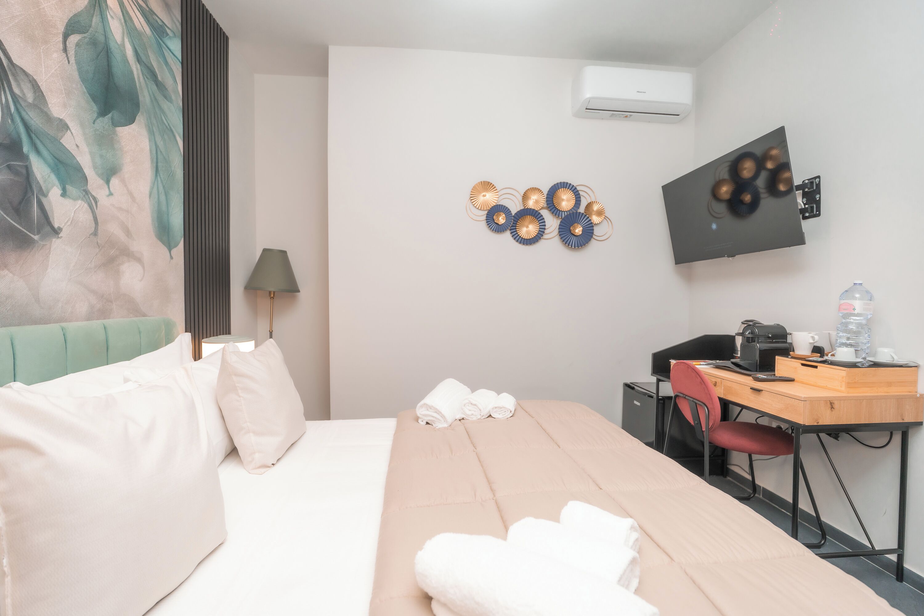 A hotel room with a bed, a desk, a chair, a TV, and a wall-mounted air conditioner.