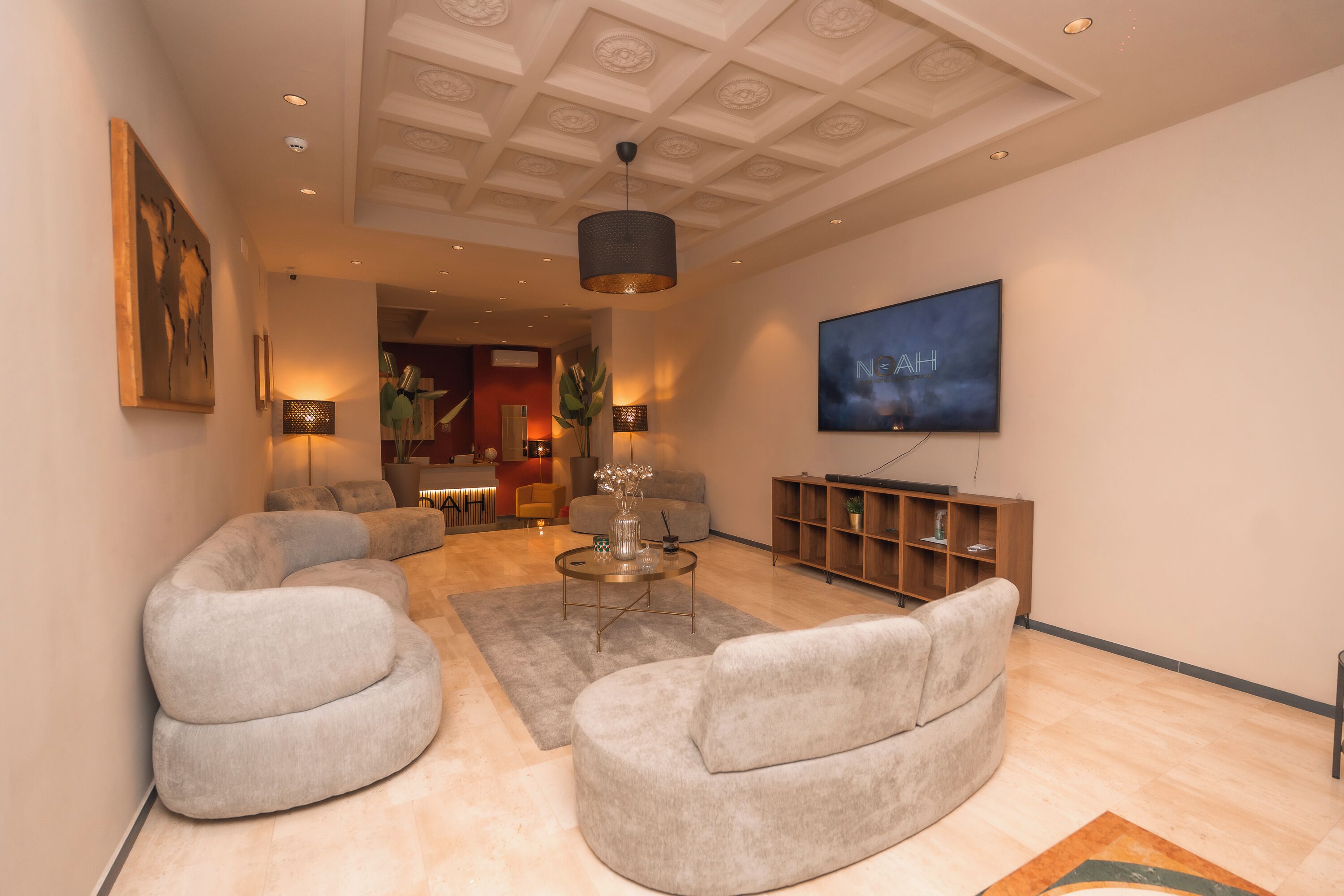 Ein modernes Wohnzimmer mit einem großen Flachbildfernseher an der Wand, einem runden Couchtisch und zwei grauen Sesseln.