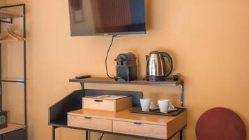 A hotel room with a bed, a desk with a kettle, cups, and a television on the wall.