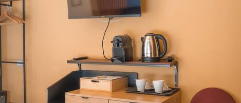 A hotel room with a bed, a desk with a kettle, cups, and a television on the wall.
