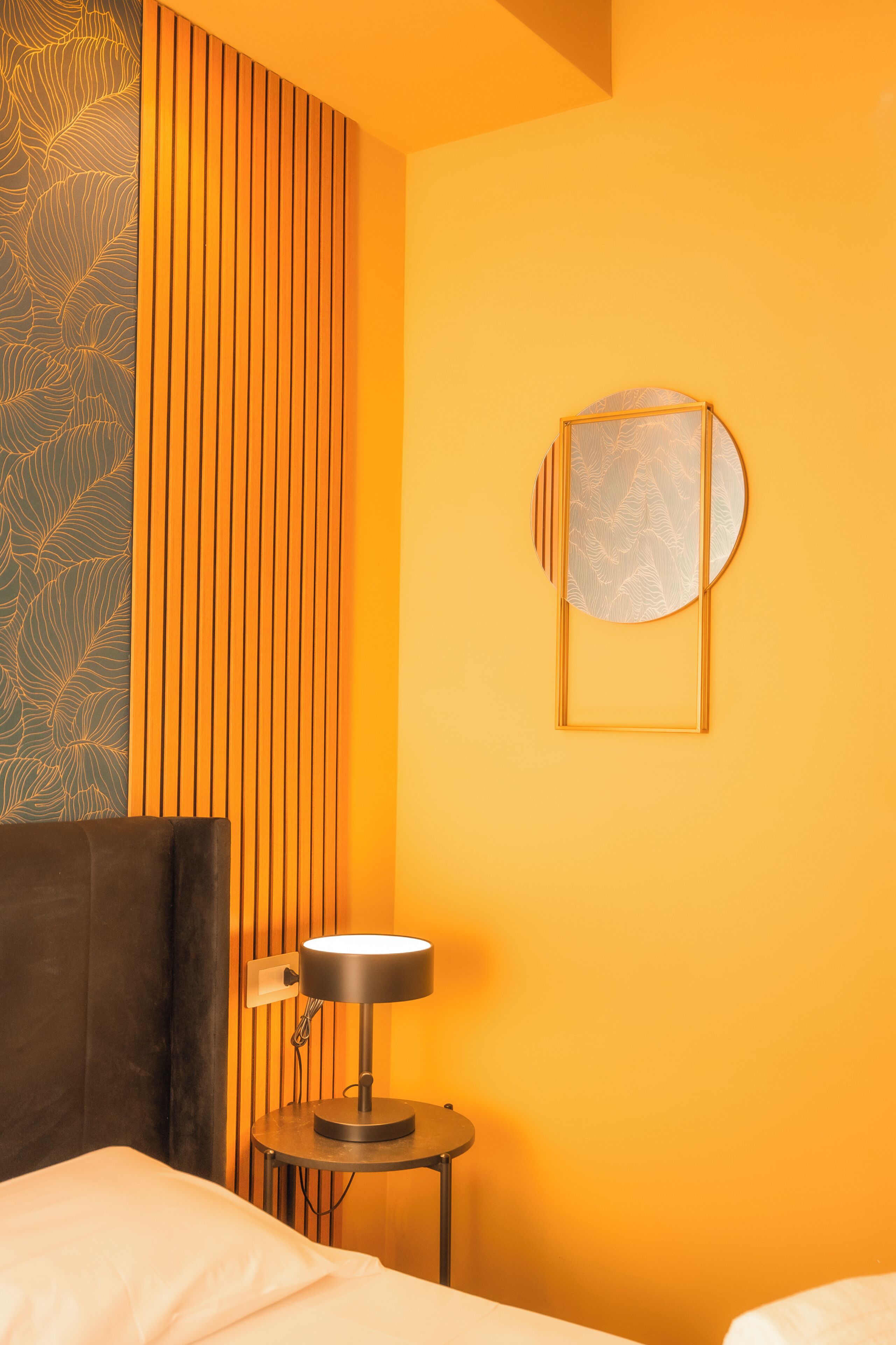 Habitación de hotel con cama, mesita de noche con lámpara, pared con listones de madera y una obra de arte enmarcada.