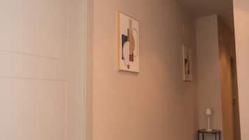 Un pasillo con una puerta blanca, una mesita con una lámpara y dos cuadros en la pared.