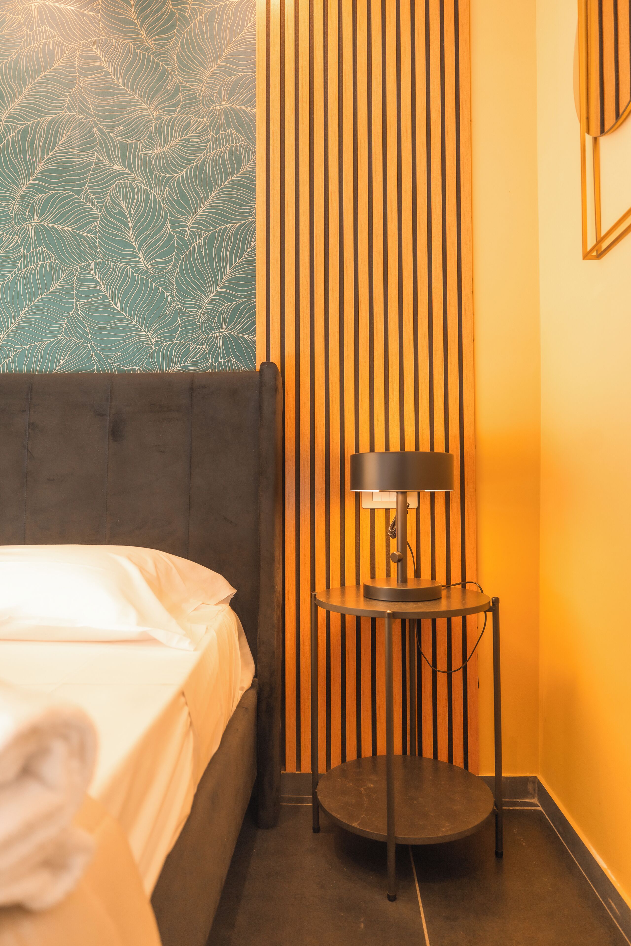 Una habitación de hotel con cama, una mesa redonda con lámpara, un panel de madera vertical y una pared con diseño.