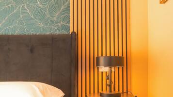 Una habitación de hotel con cama, una mesa redonda con lámpara, un panel de madera vertical y una pared con diseño.