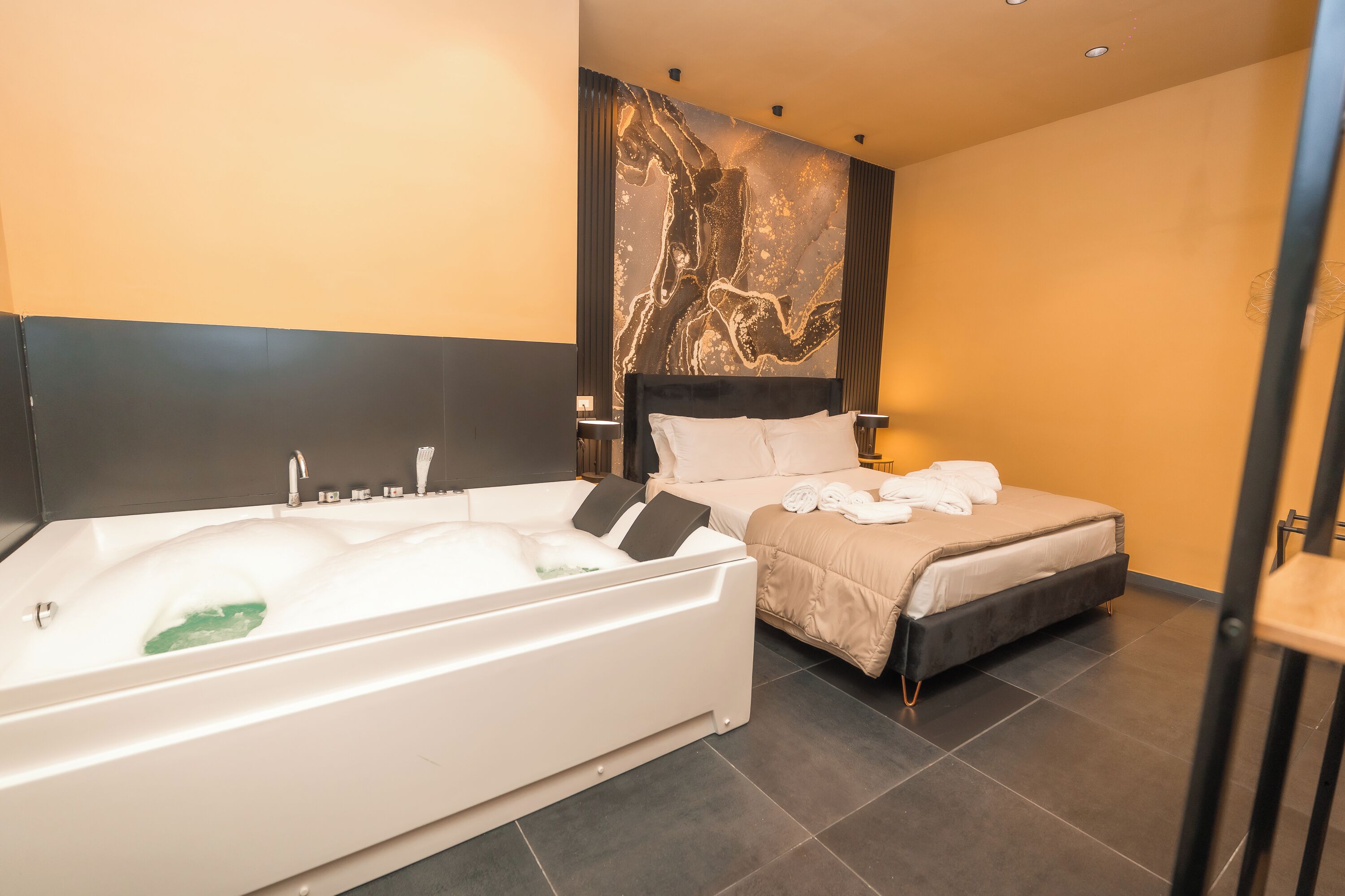 A modern hotel room with a large bathtub, a bed with a headboard, and a wall-mounted artwork.