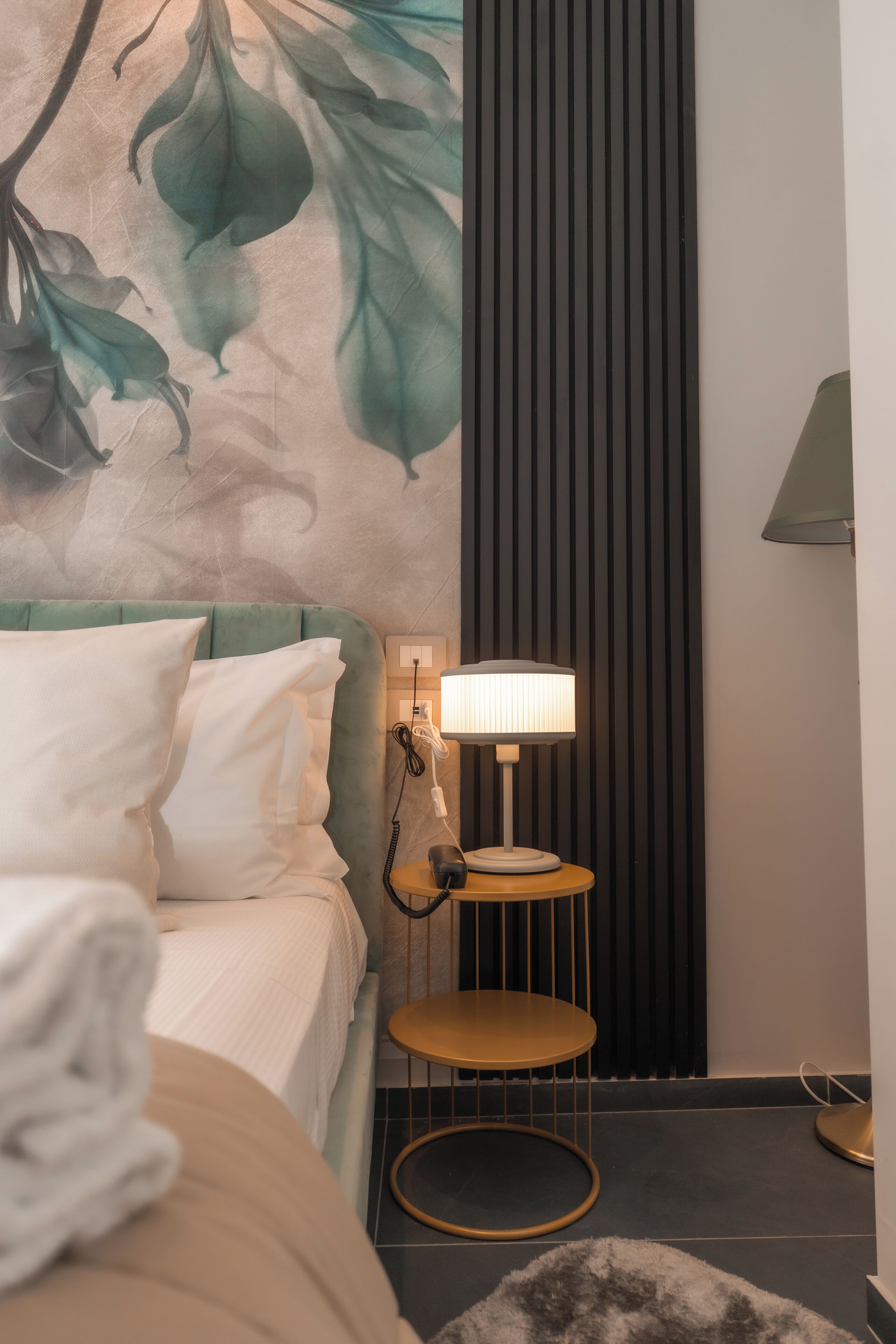 A hotel room with a bed, a wall-mounted lamp, and a small table with a lamp.