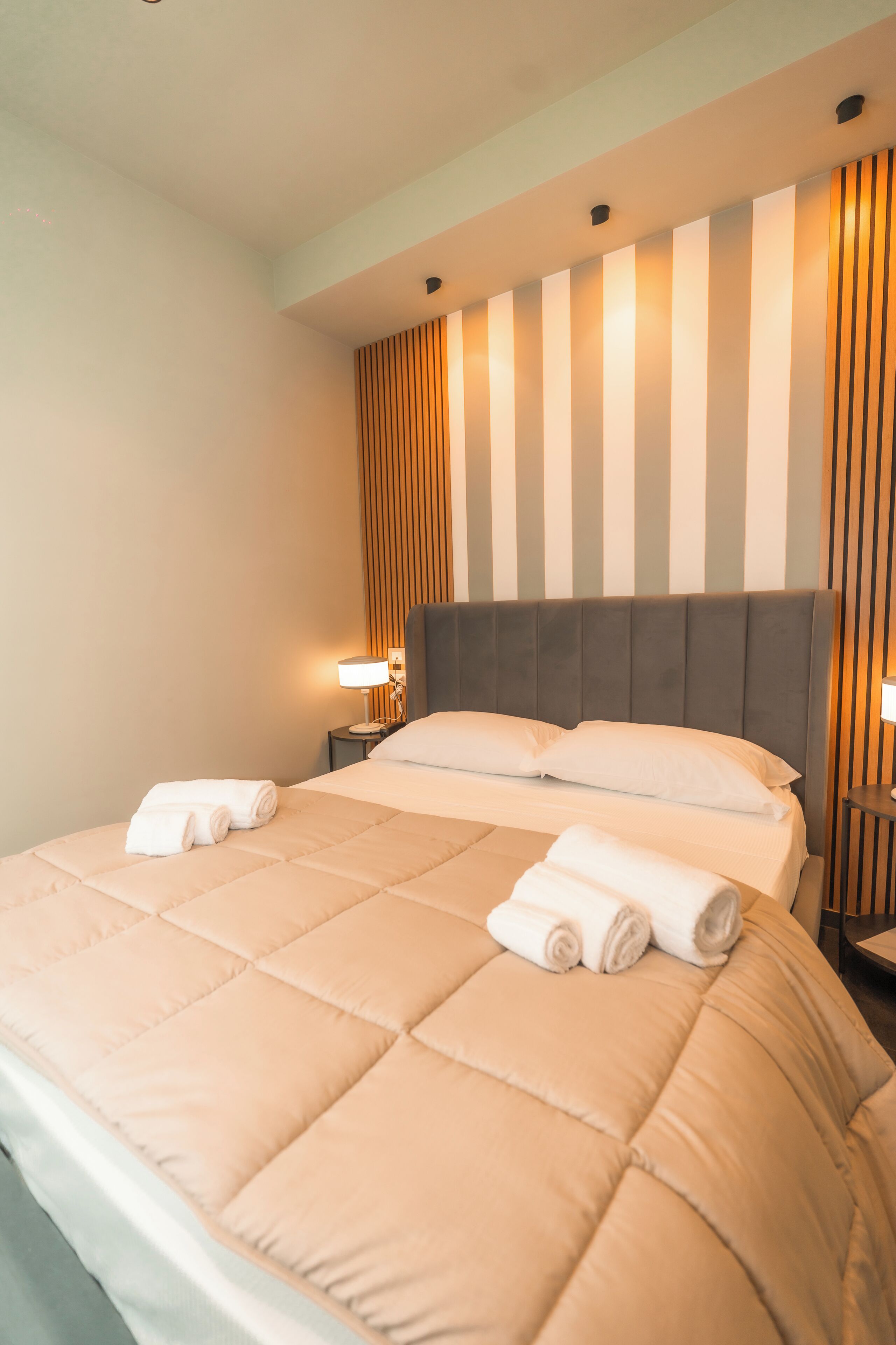 A hotel room with a large bed, two bedside tables, and a headboard with vertical slats.