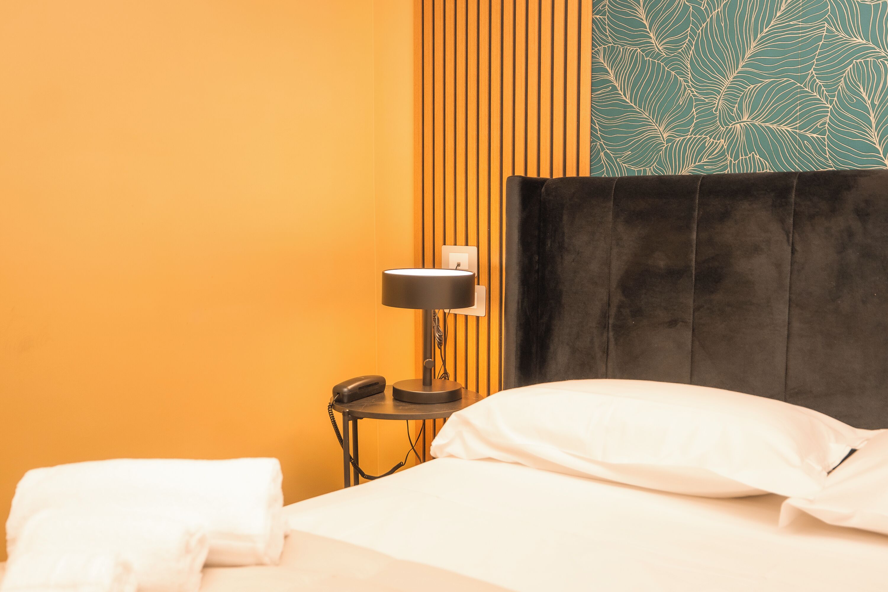 Una habitación de hotel con una cama, una mesita de noche con lámpara y un teléfono.