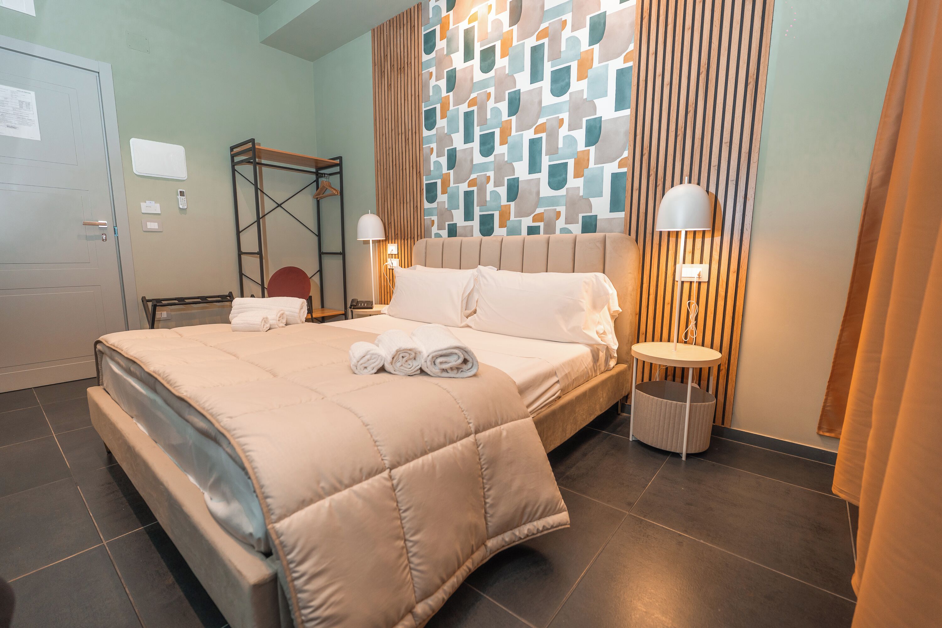 Een hotelkamer met een groot bed, twee bedlampen, een houten hoofdeinde en een behang met een patroon.