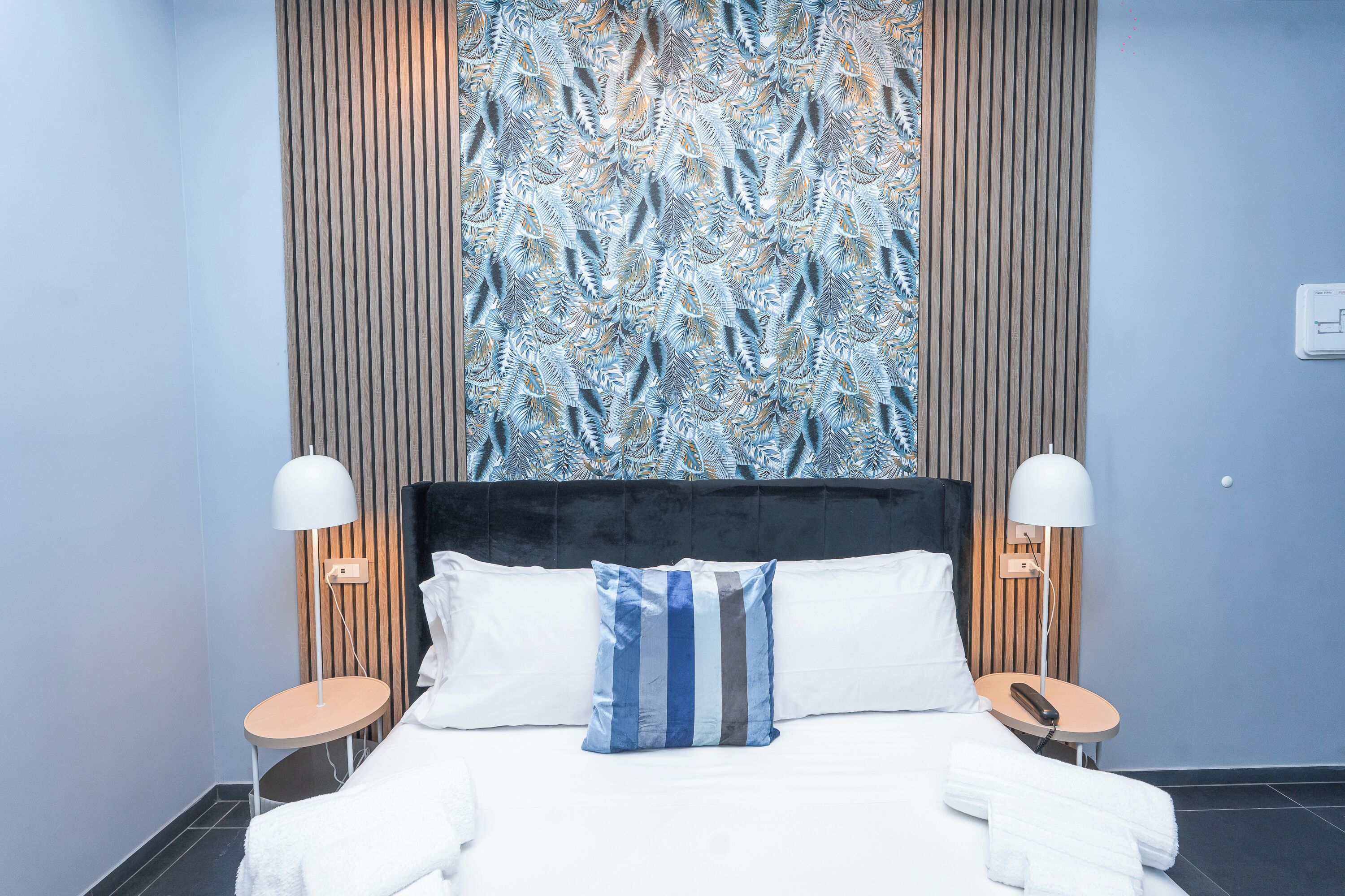 Habitación de hotel con una cama grande, dos mesitas de noche, cabecero y una pared con diseño de hojas.