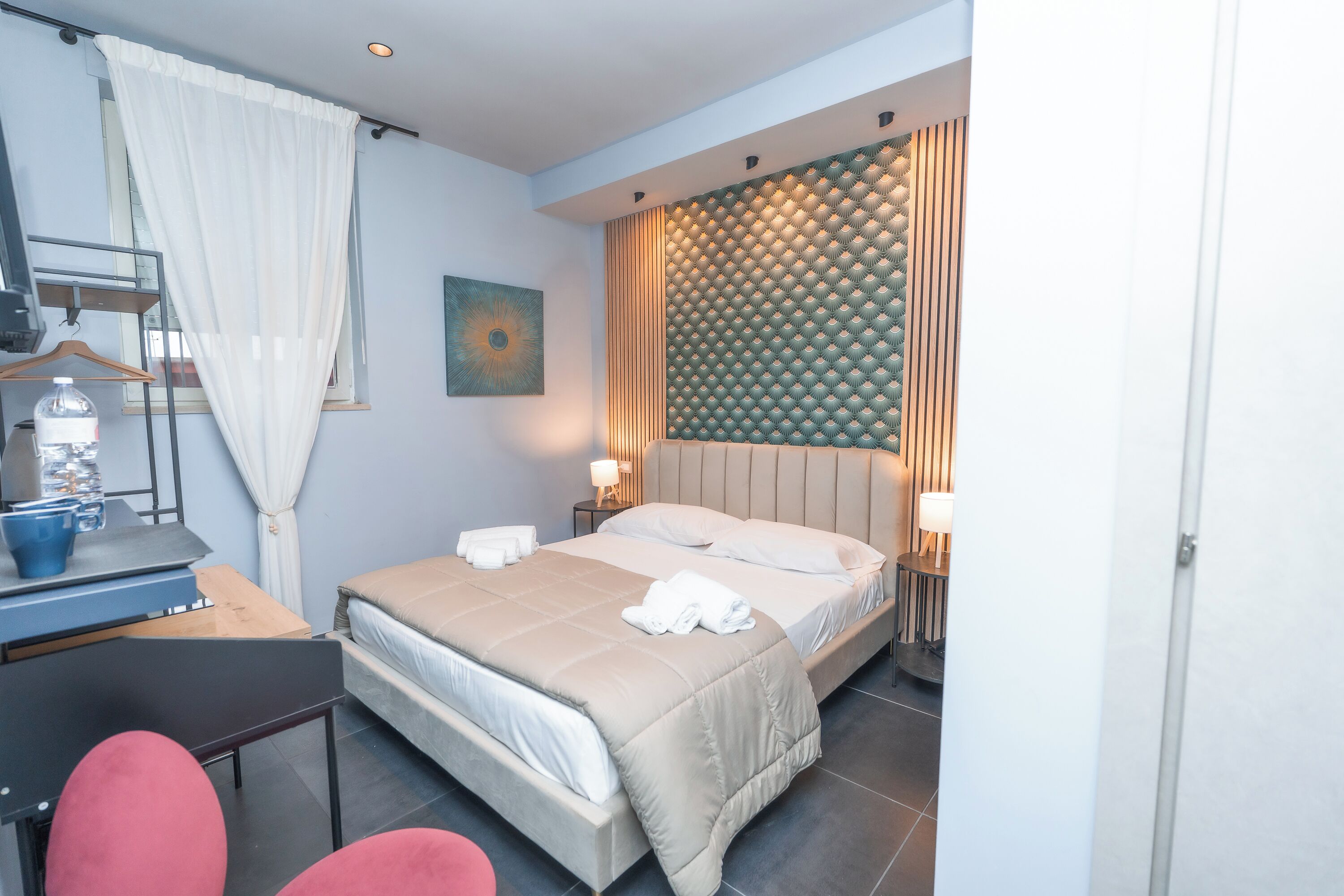 A hotel room with a bed, bedside tables, a desk, a chair, and a water bottle.