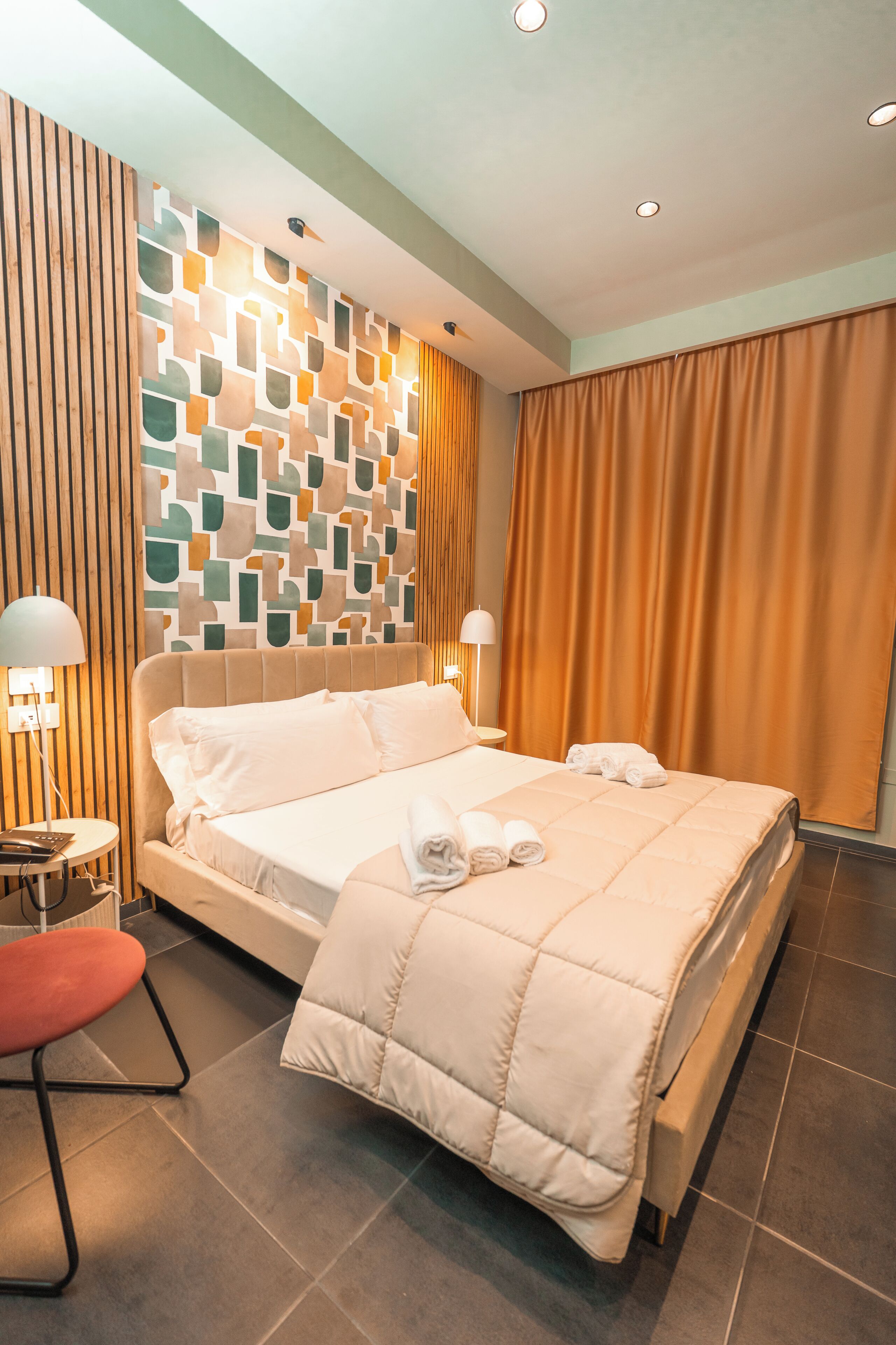 A modern hotel room with a large bed, a wooden slat wall, and a view of the city.