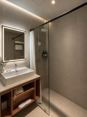 A modern bathroom with a glass shower enclosure, a large mirror, and a wooden vanity with a sink. - Asaya Kata Beach Pre-Opening (Karon)