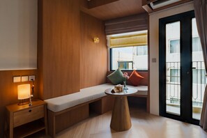 Una camera d'albergo con una panca di legno, un comodino con una lampada, un tavolino con un vaso e una finestra vista edifici.