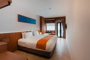 A hotel room with a large bed, a desk, a chair, a window with a view, and a door leading to a balcony. - Asaya Kata Beach Pre-Opening (Karon)