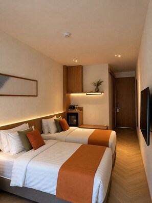 A hotel room with two beds, a bedside table with a lamp, a small cabinet, and a wall-mounted TV. - Asaya Kata (Karon)
