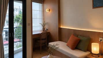 Ein Hotelzimmer mit Holzboden, einer Couch mit Kissen, einem kleinen Tisch mit Vase und Schale, einem Schreibtisch mit Stuhl und einem Fenster mit Vorhängen.