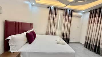 Quarto de hotel com uma cama grande, um ventilador de teto e cortinas.