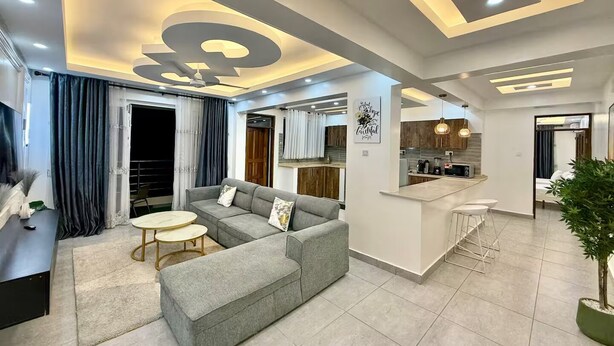 Ein modernes Wohnzimmer mit einem grauen Ecksofa, einem kleinen runden Tisch und einer Bar mit Barhocker.
