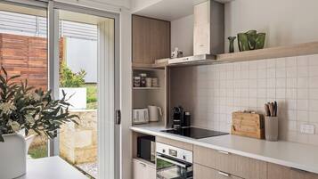Une cuisine moderne dotée d’une porte-fenêtre coulissante donnant sur un patio, d’appareils électroménagers intégrés et d’un plan de travail en bois.