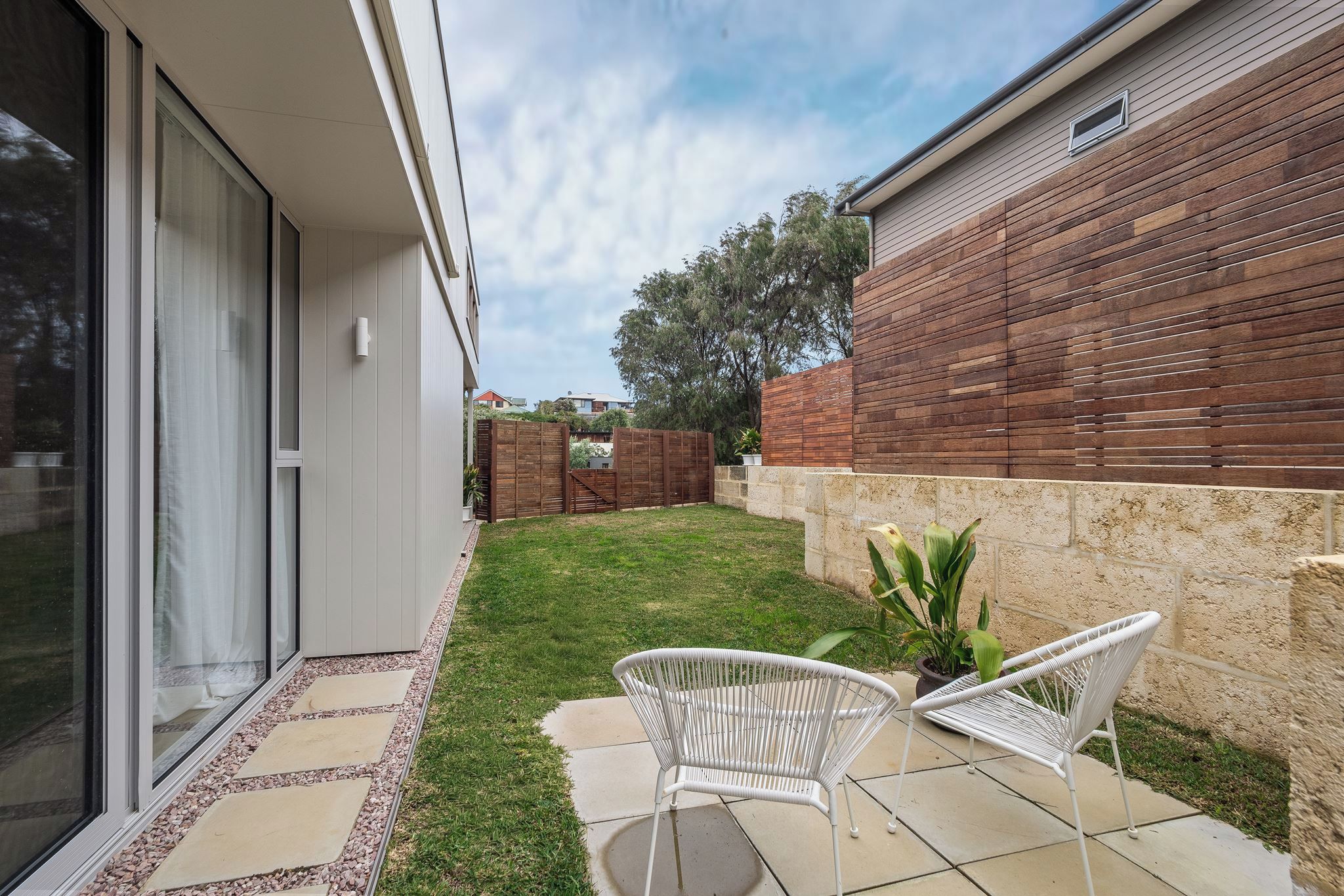 Un espace patio avec une chaise blanche, une plante en pot et une clôture en bois.