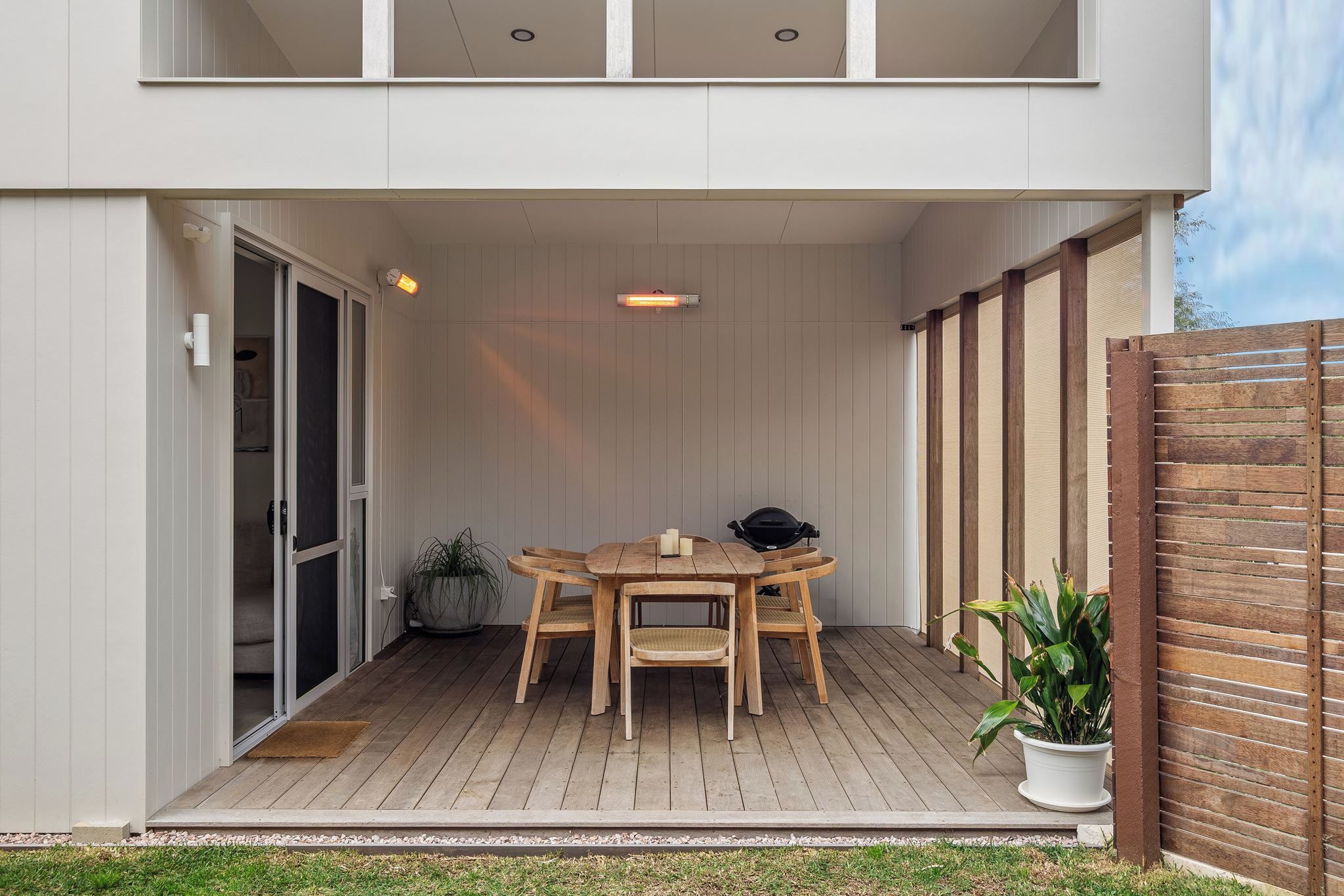 A patio with a wooden table and chairs, a potted plant, and a sliding glass door.
