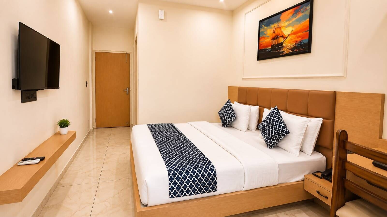 A hotel room with a bed, a TV, a painting, and a wooden bench.