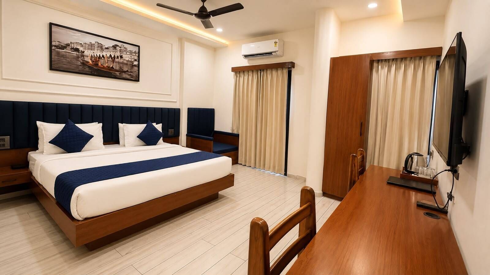 A hotel room with a bed, a desk, a television, an air conditioner, and a picture on the wall.