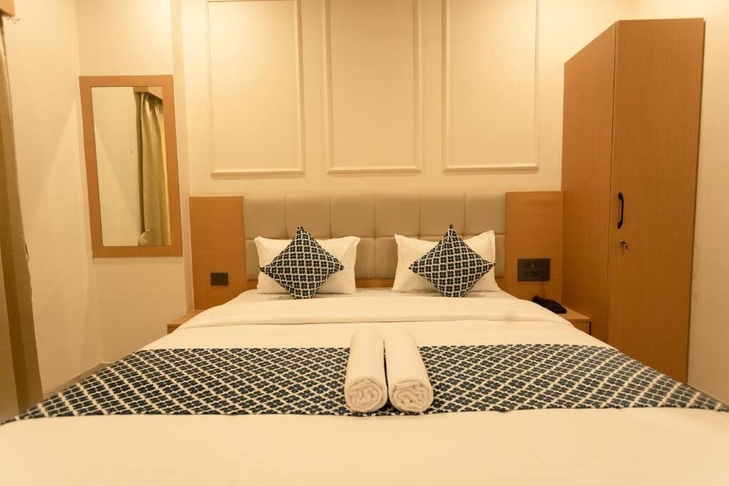 A hotel room with a large bed, two pillows, a bedside table, a nightstand, a wardrobe, and a mirror.