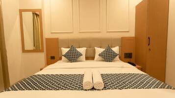 A hotel room with a large bed, two pillows, a bedside table, a nightstand, a wardrobe, and a mirror.