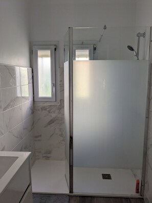 A modern bathroom with a glass-enclosed shower, a marble-tiled wall, and a small window.