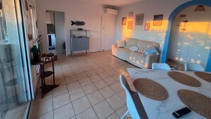 A spacious living area with a sofa, a dining table with placemats, a ceiling fan, and a kitchen in the background.