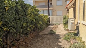 A gravel path leading to a building with a balcony, surrounded by dense shrubbery.