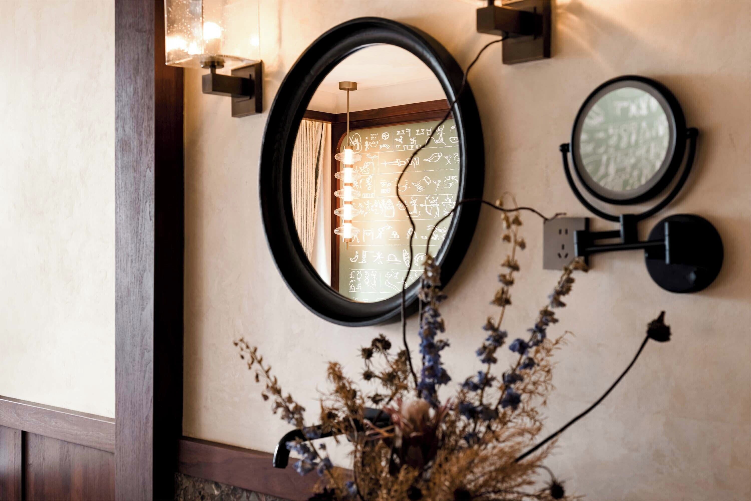 A wall-mounted mirror with a circular frame, a wall-mounted light fixture, and a small round mirror.
