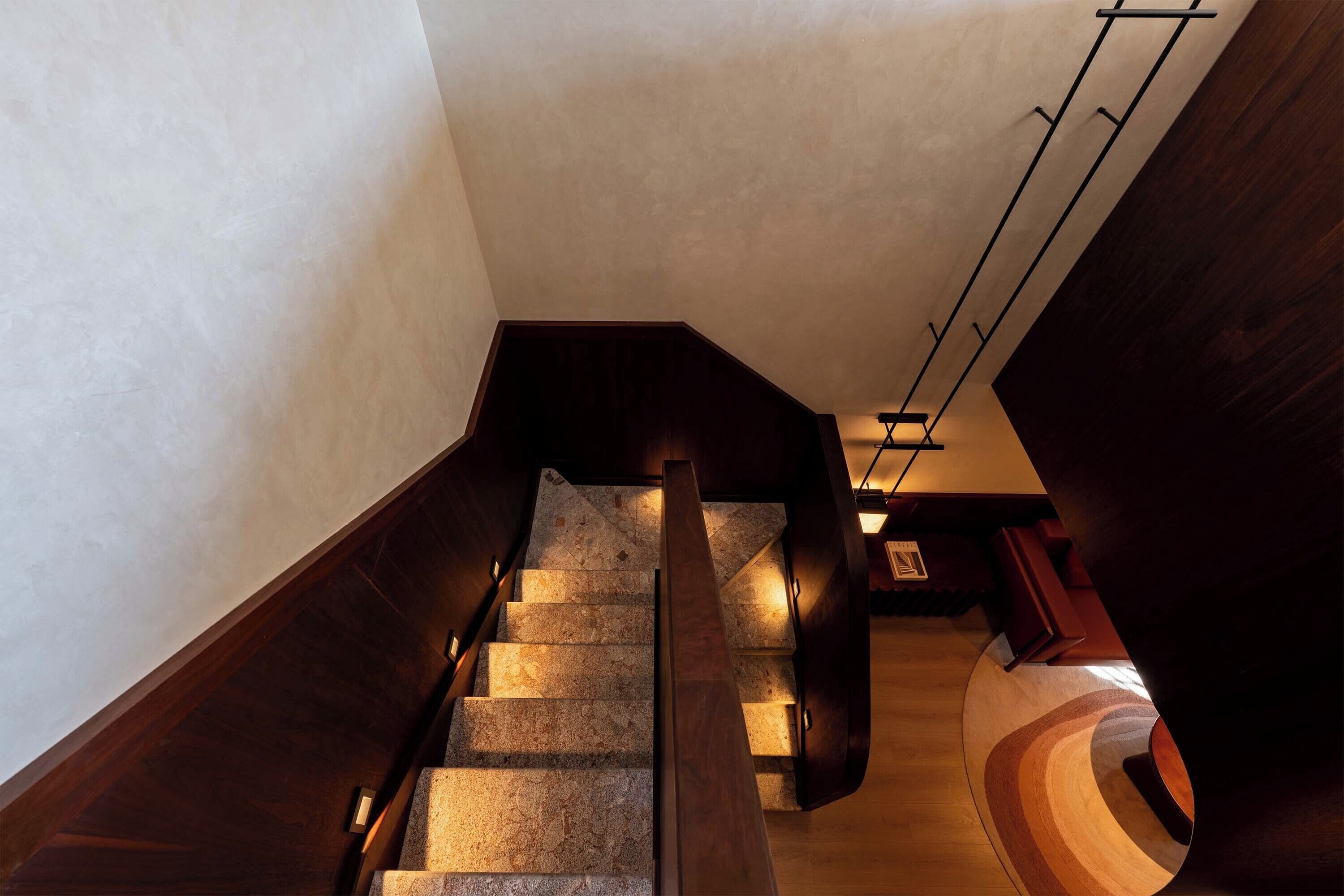 A modern staircase with wooden handrails and stone steps, leading to a lower level with a curved wooden floor.