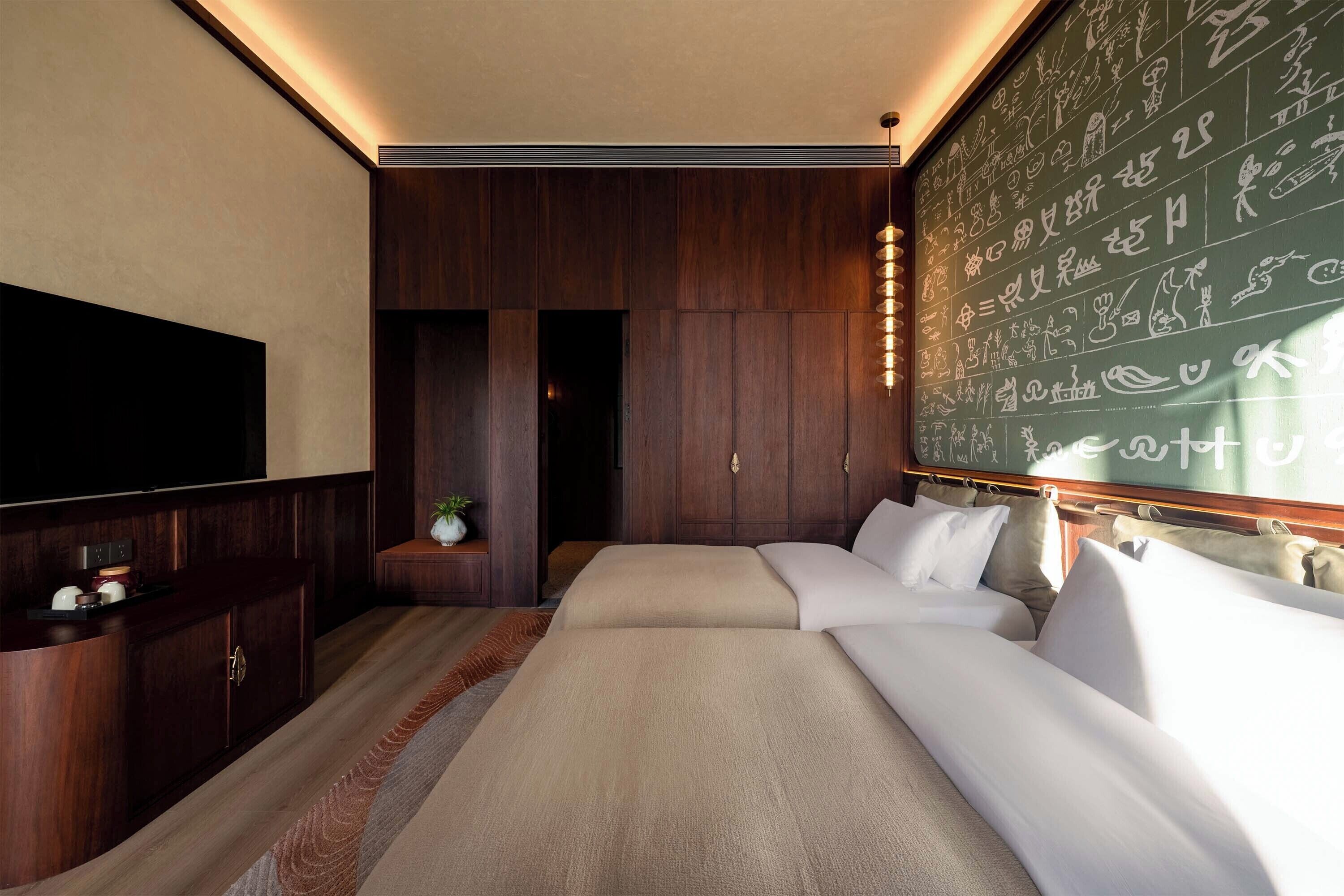 Hotelkamer met een groot bed, een flatscreen televisie aan de muur en een houten paneelwand met kalligrafie.