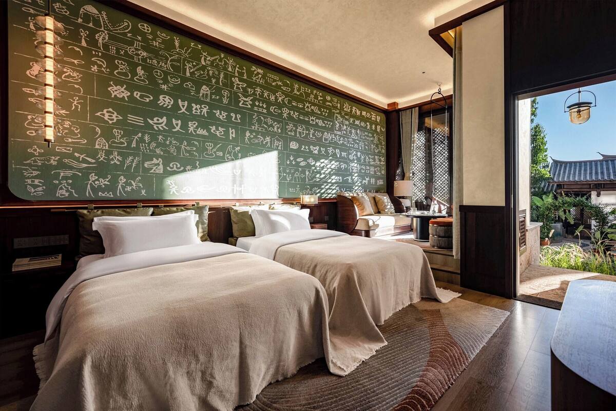 Ein Hotelzimmer mit zwei Betten, einer großen Wand mit Kalligraphie und Blick auf traditionelle Architektur.