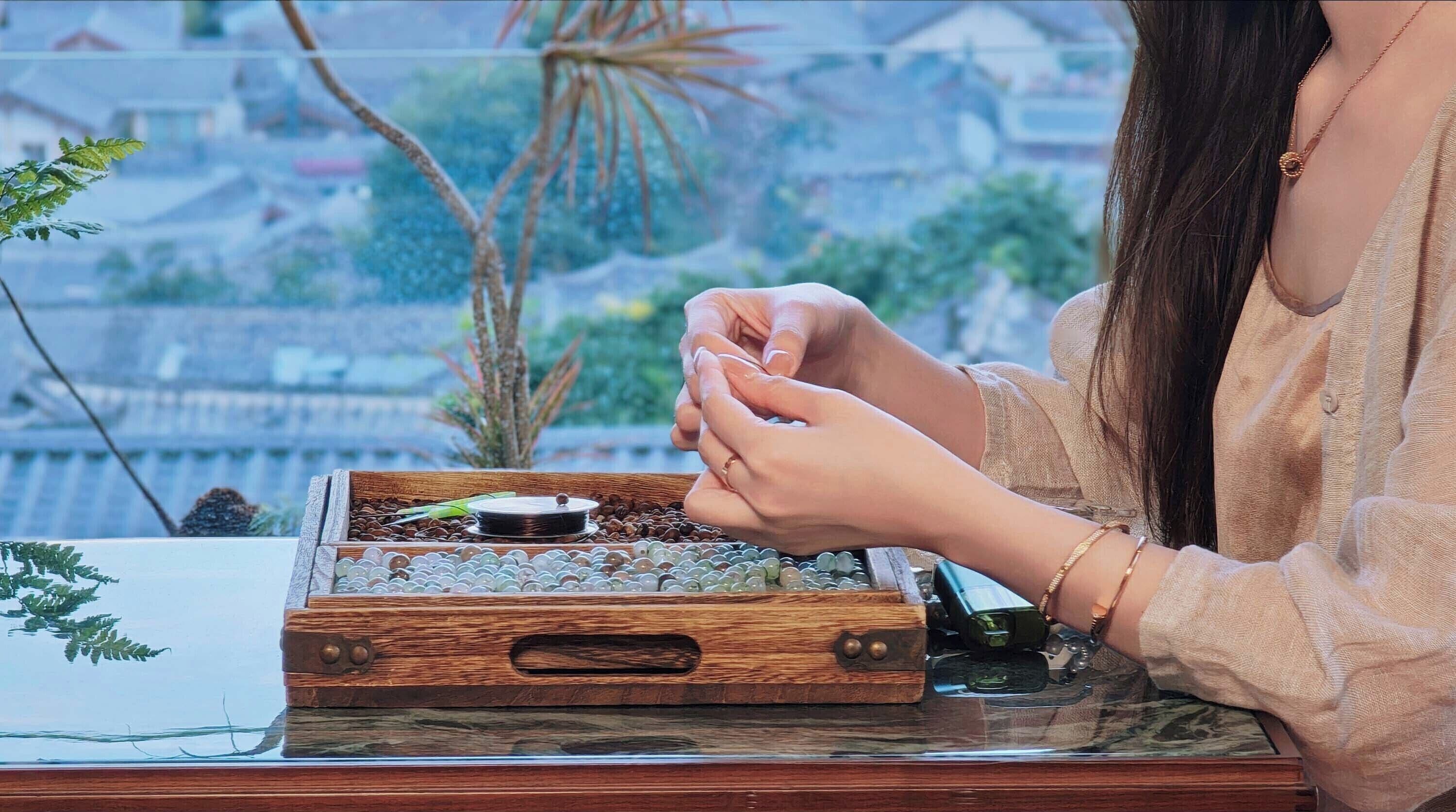 A person sitting at a wooden table with a glass surface, holding a small object.