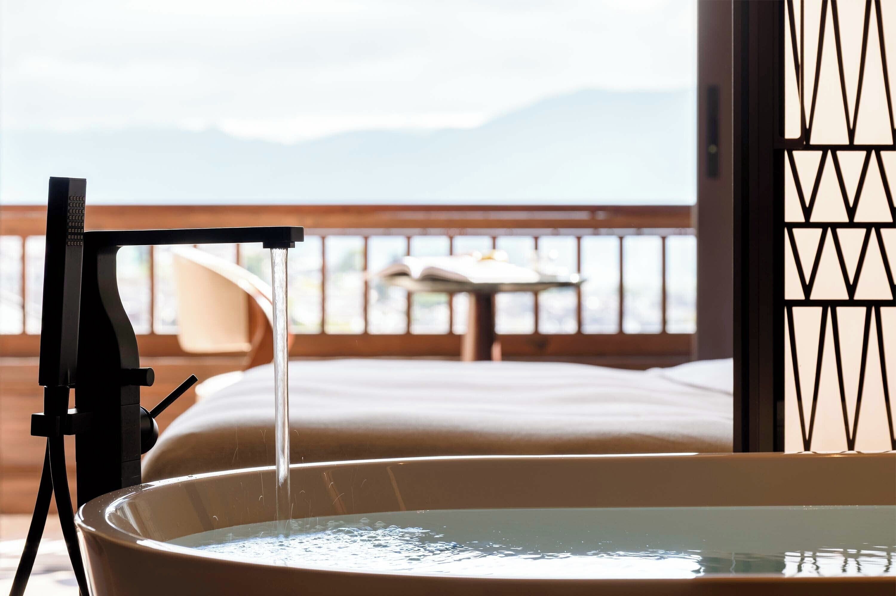 A bathtub with running water, a wooden railing, and a view of mountains in the background.