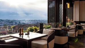 Un comedor con una mesa y sillas, vista de un paisaje urbano a través de un panel de vidrio y una planta decorativa.