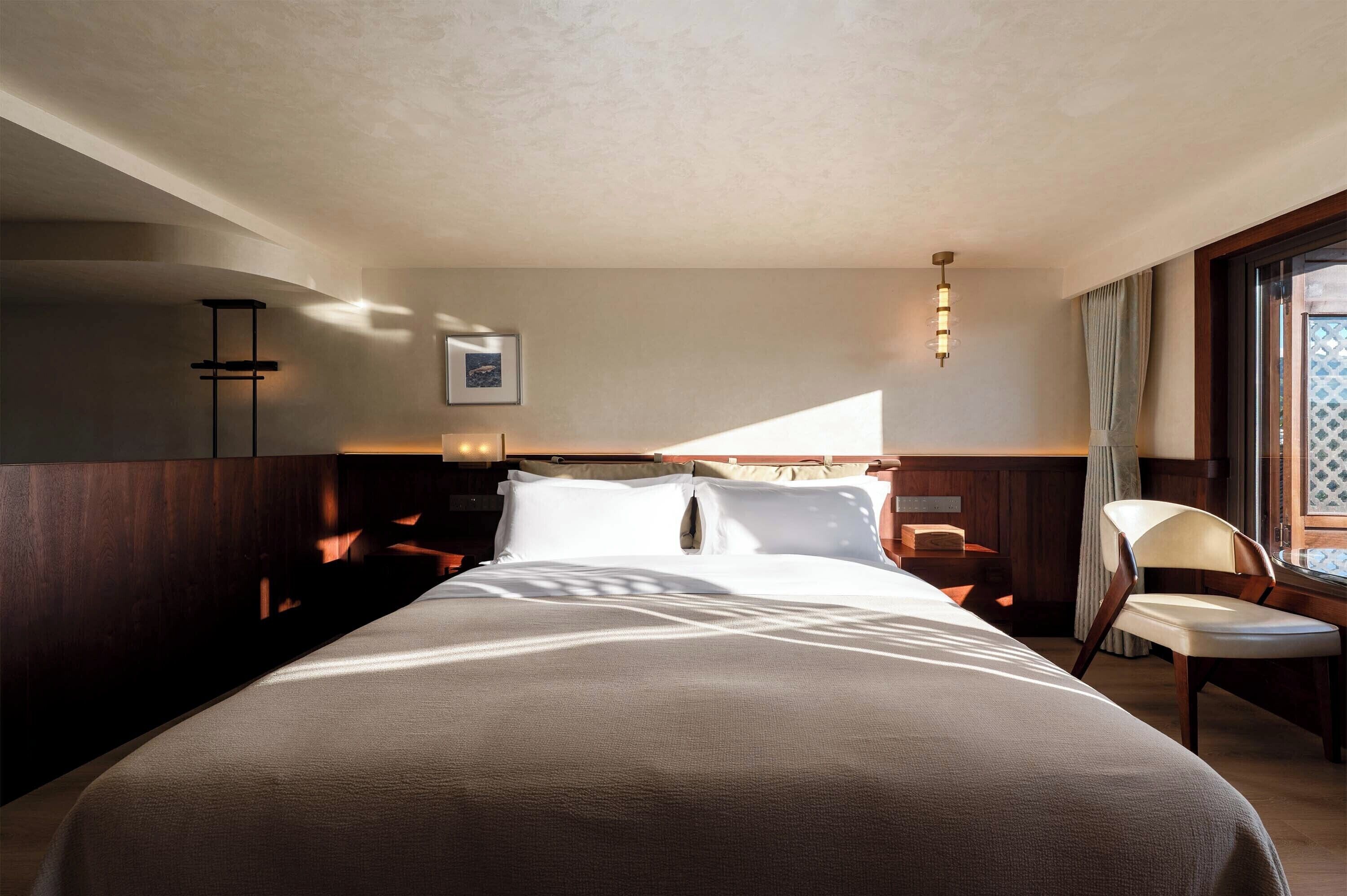 Una habitación de hotel con una cama grande, una mesita de noche, una silla y una ventana con cortinas.