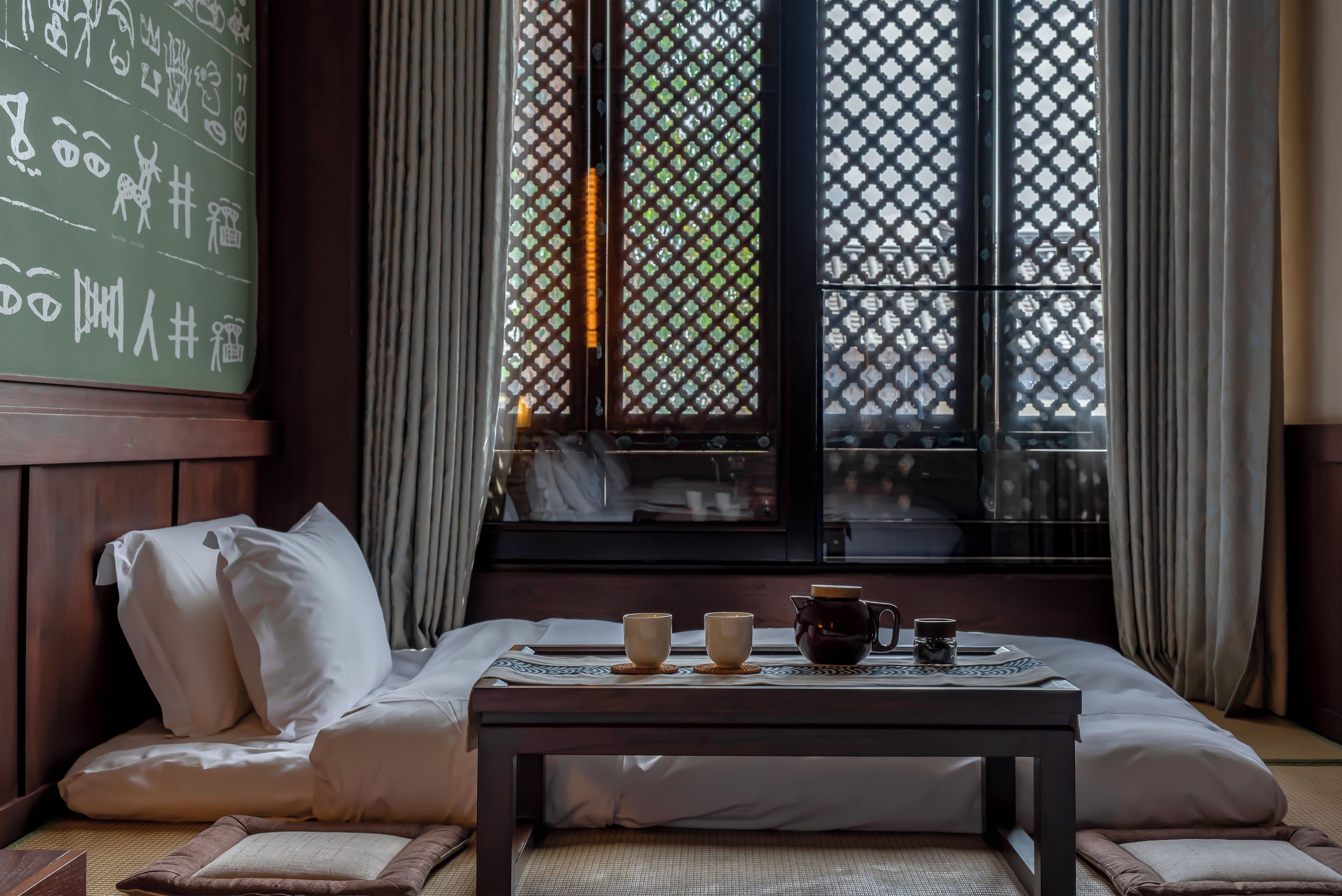 Una habitación tradicional con cama, una mesa con juego de té y una ventana con diseño de celosía.