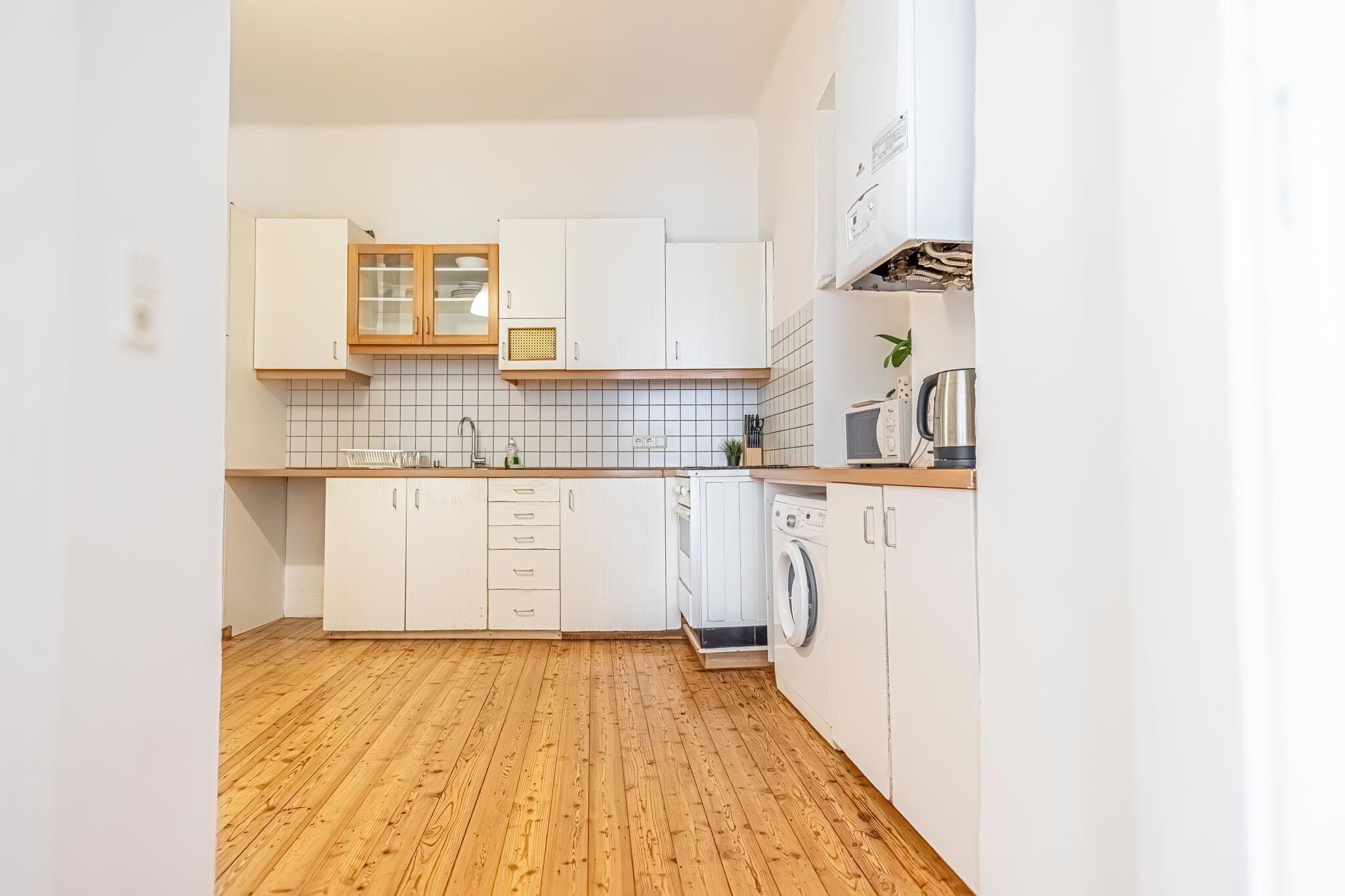 Une cuisine compacte avec des meubles blancs, un lave-linge et un four à micro-ondes.