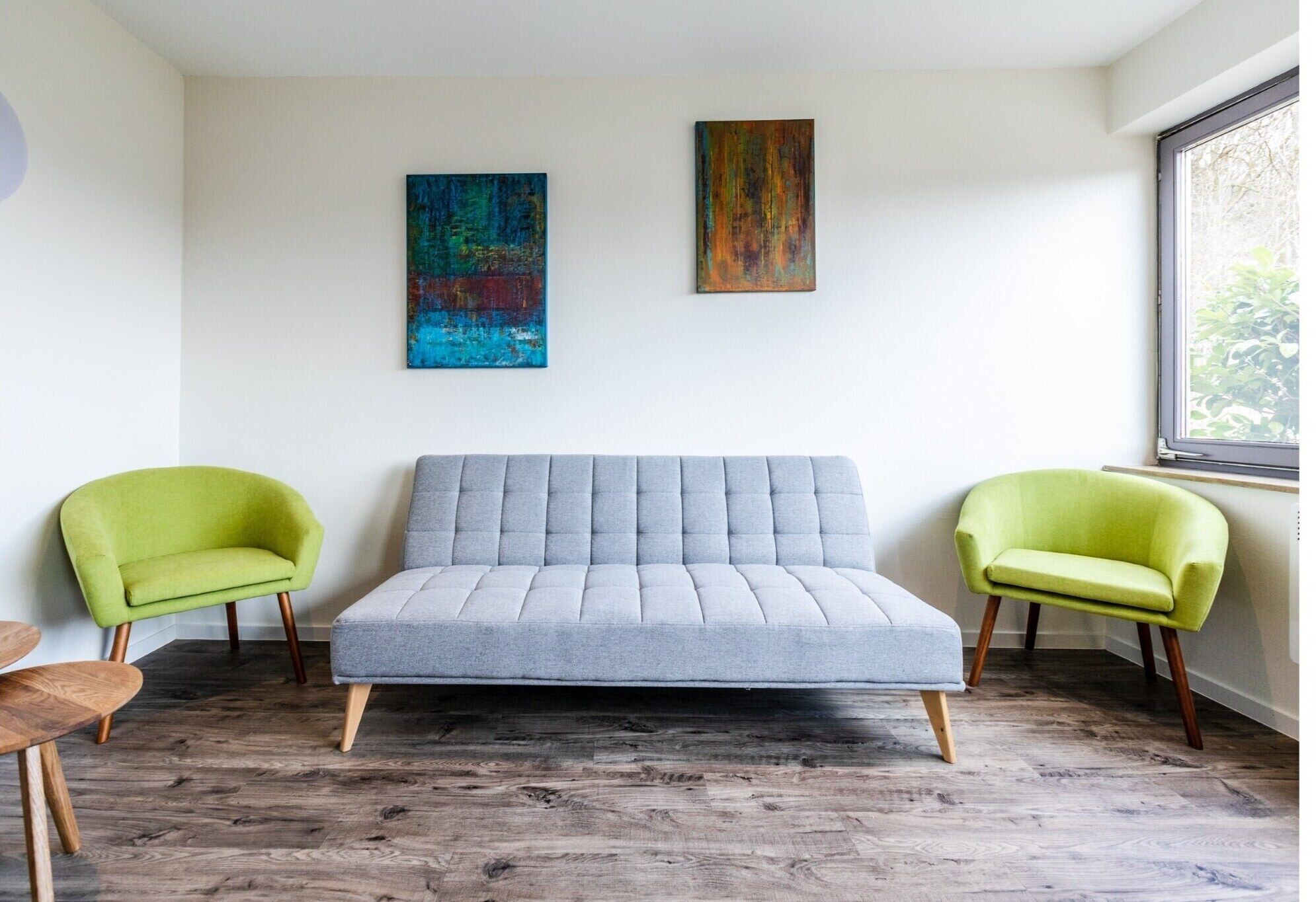 A modern room with a grey sofa, two green armchairs, and wooden flooring.