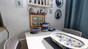 Un coin repas avec une table blanche, de la vaisselle en céramique bleue et blanche, et des œuvres d’art encadrées accrochées au mur.